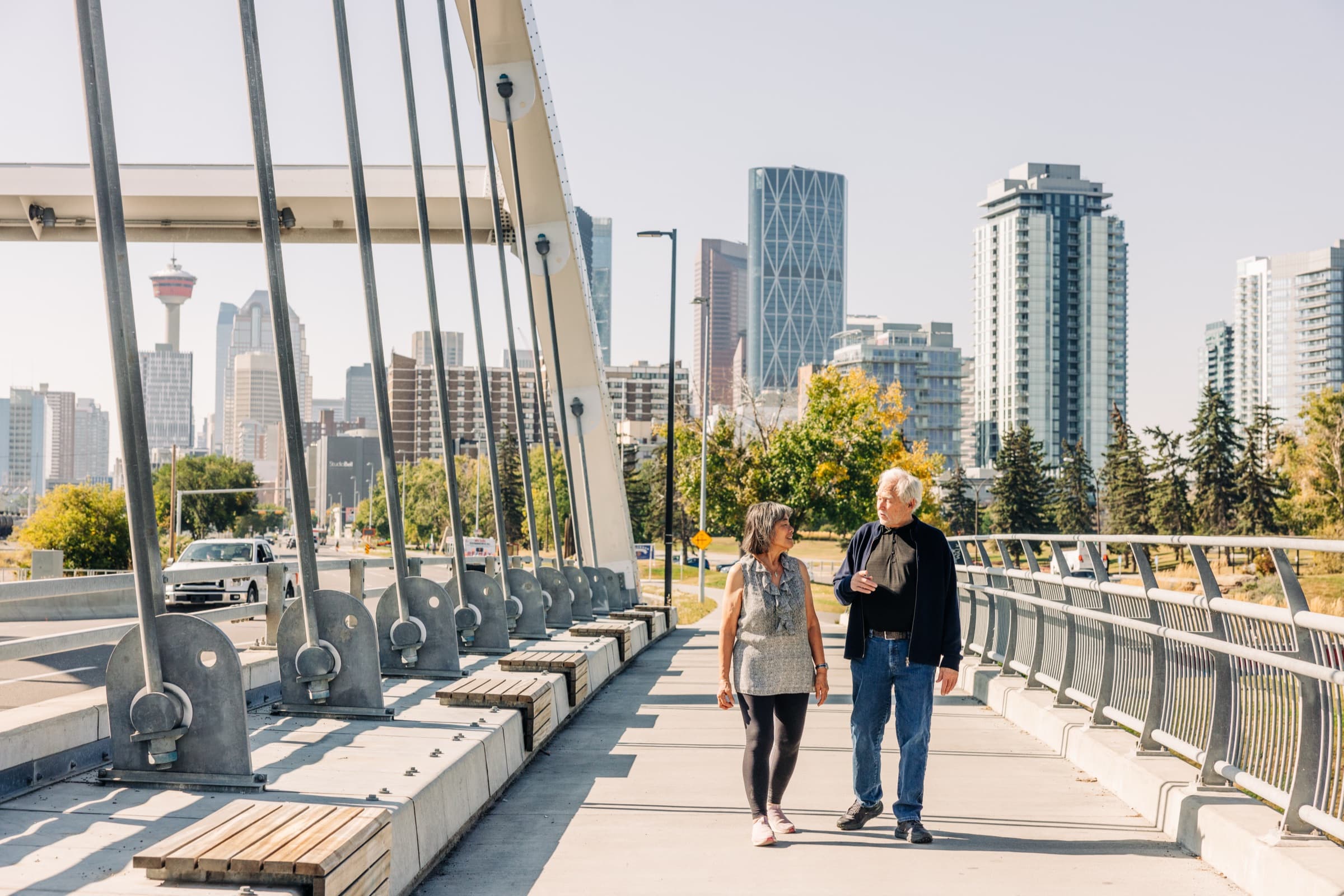 Nick and Madeline of Legacy Energy walking across a Calgary bridge with the downtown skyline behind them